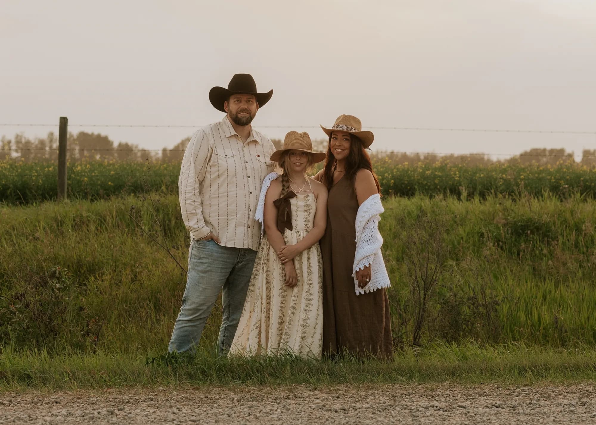 Brian, Anya and Amanda standing on a gravel road beside a summer field at sunset